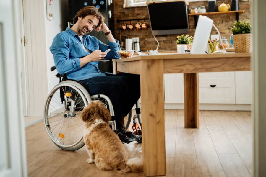 Happy disabled businessman using mobile phone while taking a break from work at home.