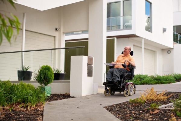 Man in an electric wheelchair on a footpath in a suburban setting.