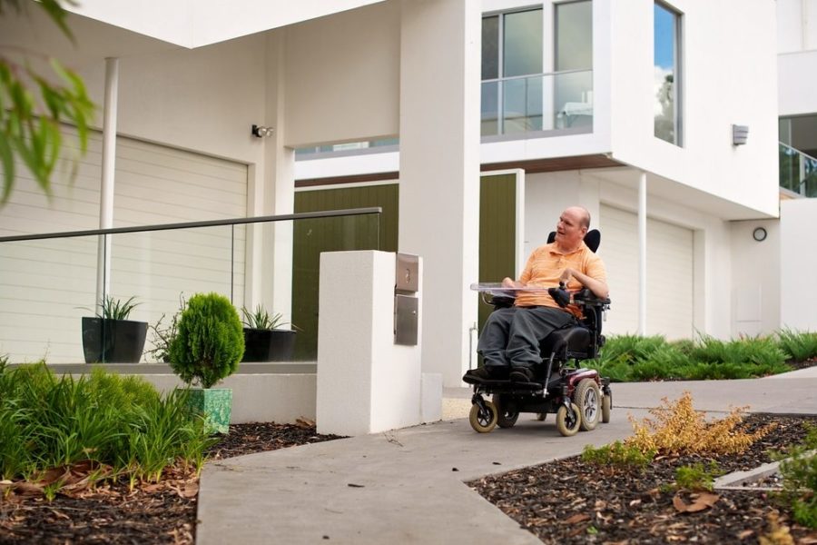 Man in an electric wheelchair on a footpath in a suburban setting.