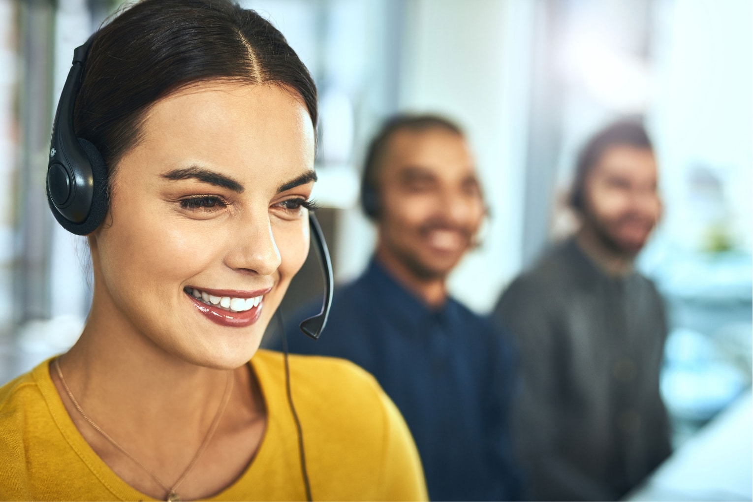 A young call female centre agent wearing yellow shirt working in an office with her colleagues in the background