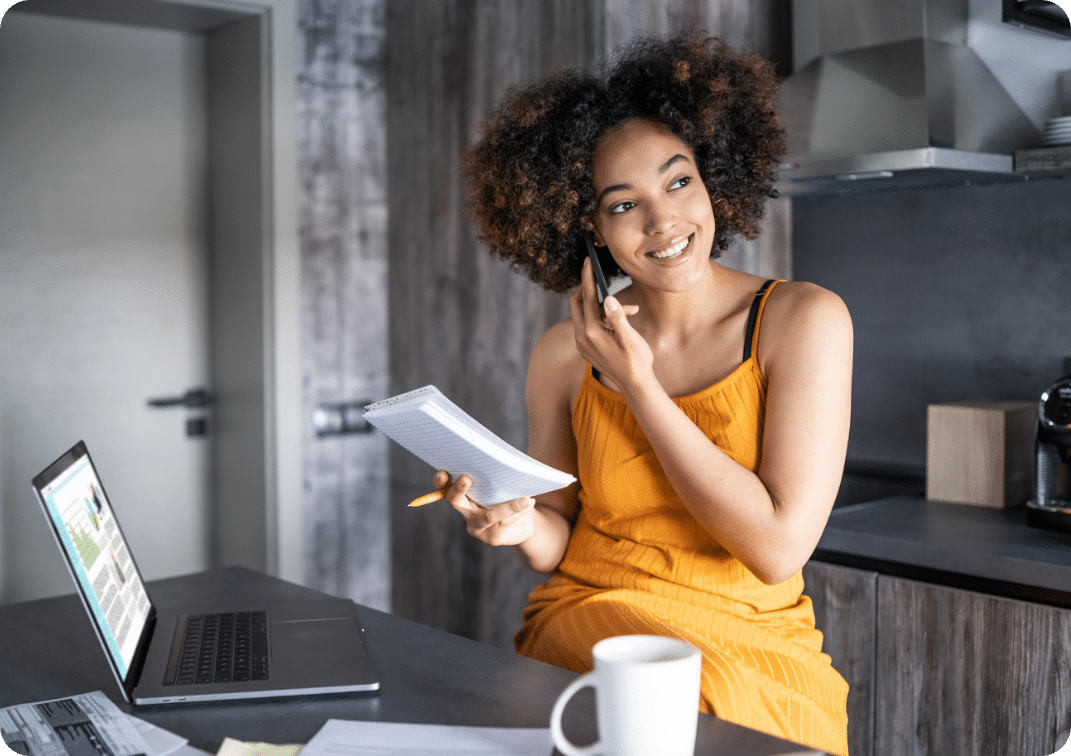 Young afro woman having a work day at home office sitting in the kitchen checking documents and talking on the phone